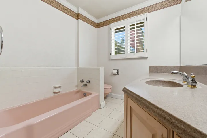Bathroom featuring a vanity with an integrated sink, a pink bathtub, and a window with white shutters