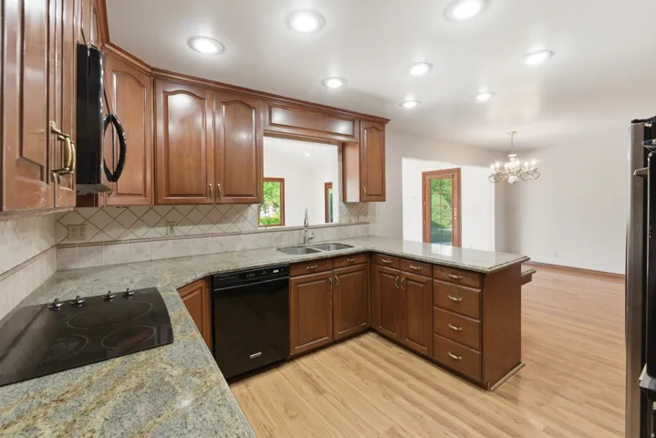 Kitchen featuring wood cabinetry, granite countertops, tile backsplash, and a black cooktop