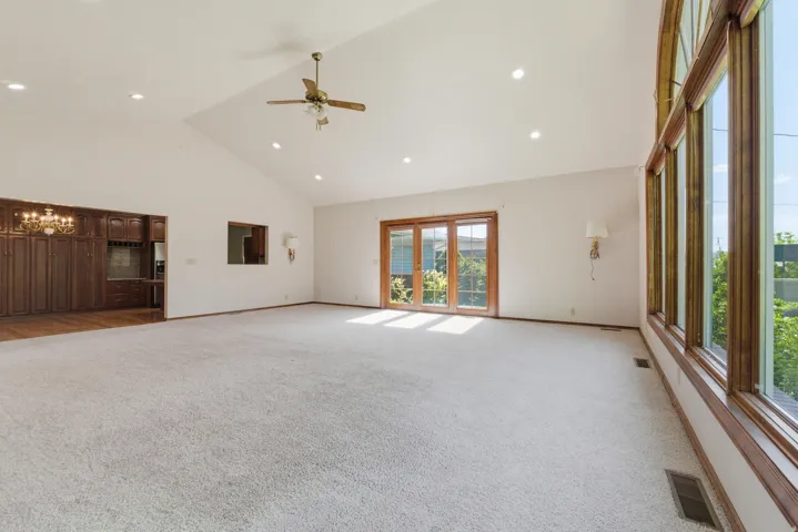 Spacious room featuring vaulted ceilings with recessed lighting and a ceiling fan, a wall of large windows, and light-toned carpeting