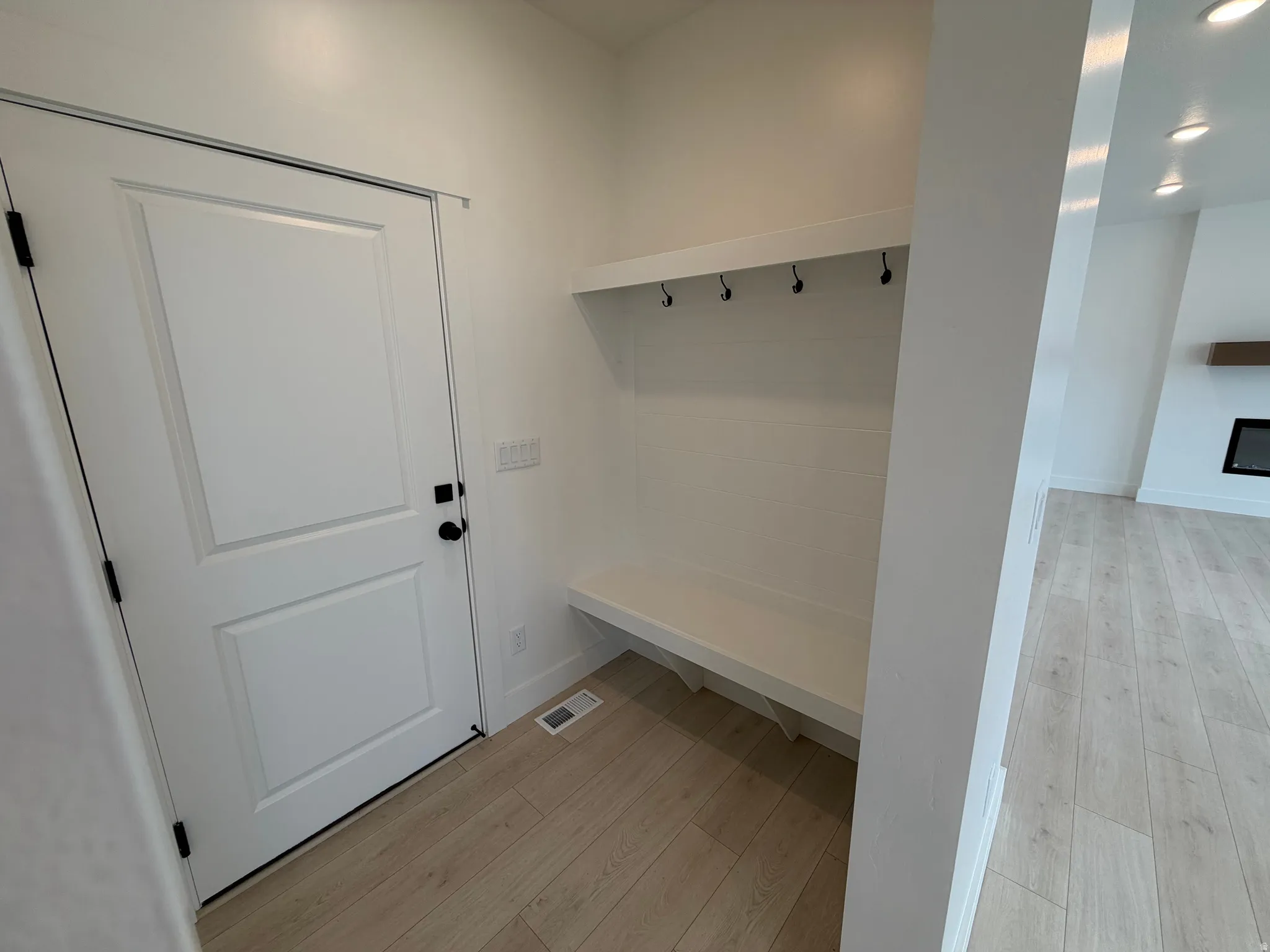 Entryway featuring built-in bench seating and coat hooks, with wood-finish flooring extending into the interior