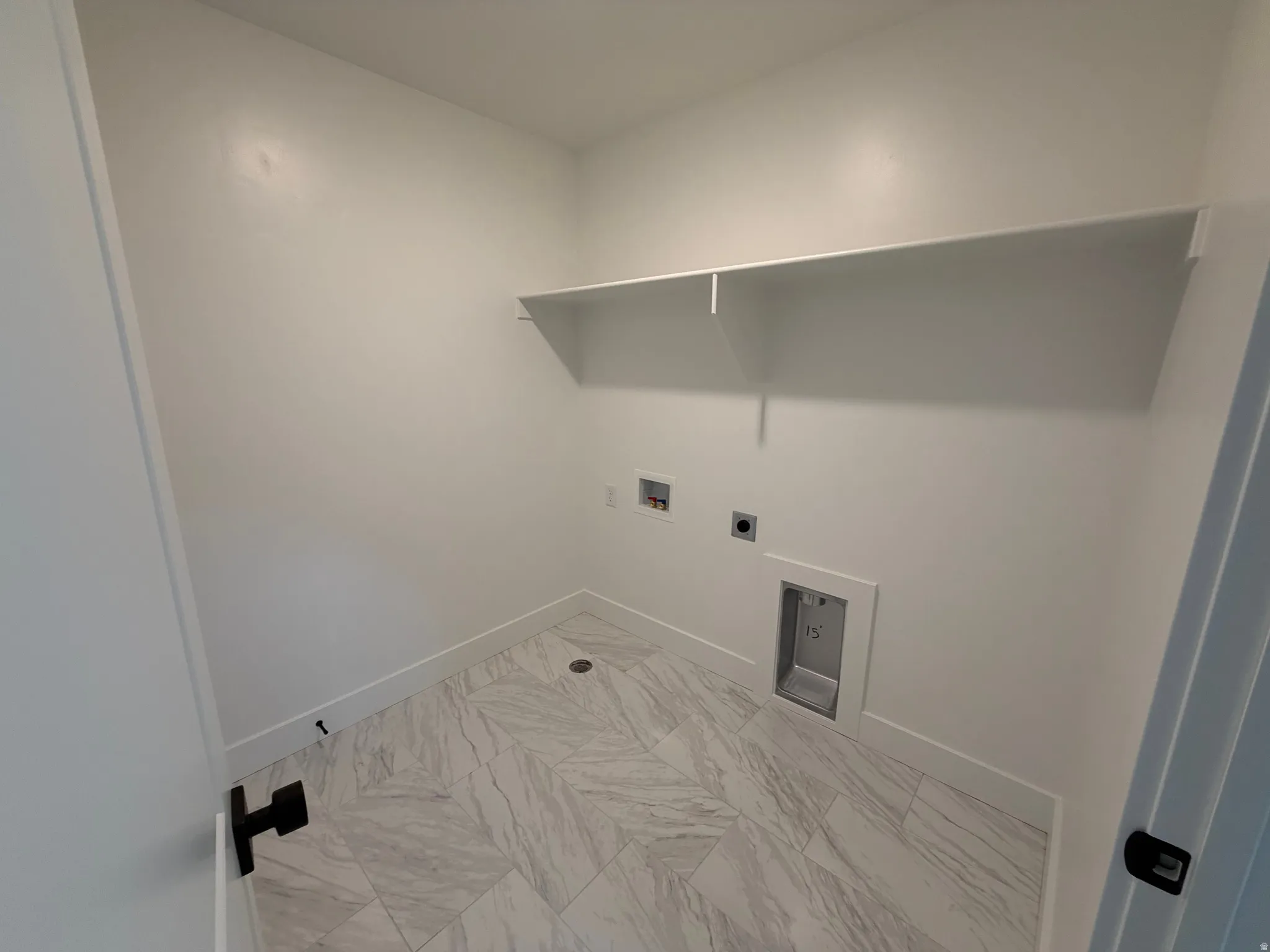 Dedicated utility space with contemporary marble-look tile flooring, crisp white walls, and an integrated wall-mounted shelf