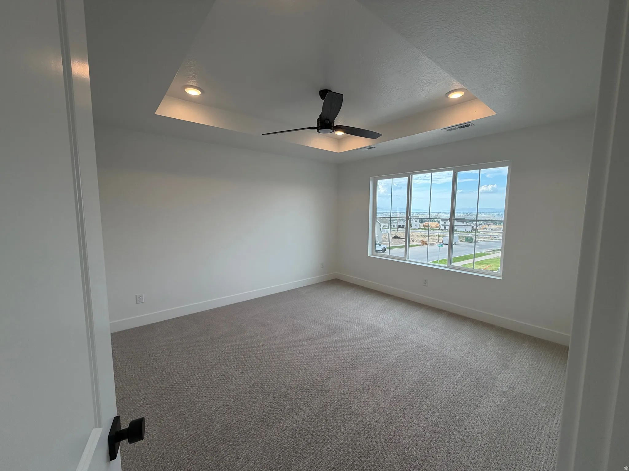 Spacious room with a tray ceiling featuring recessed lighting and a ceiling fan