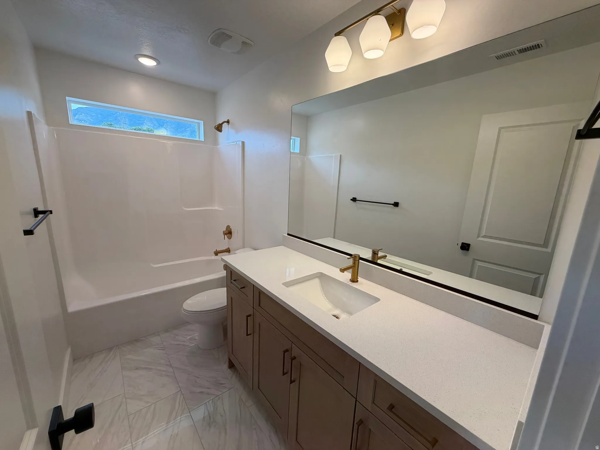 Modern bathroom featuring a wood-finish vanity with a light countertop, an integrated sink, and a gold-finish faucet