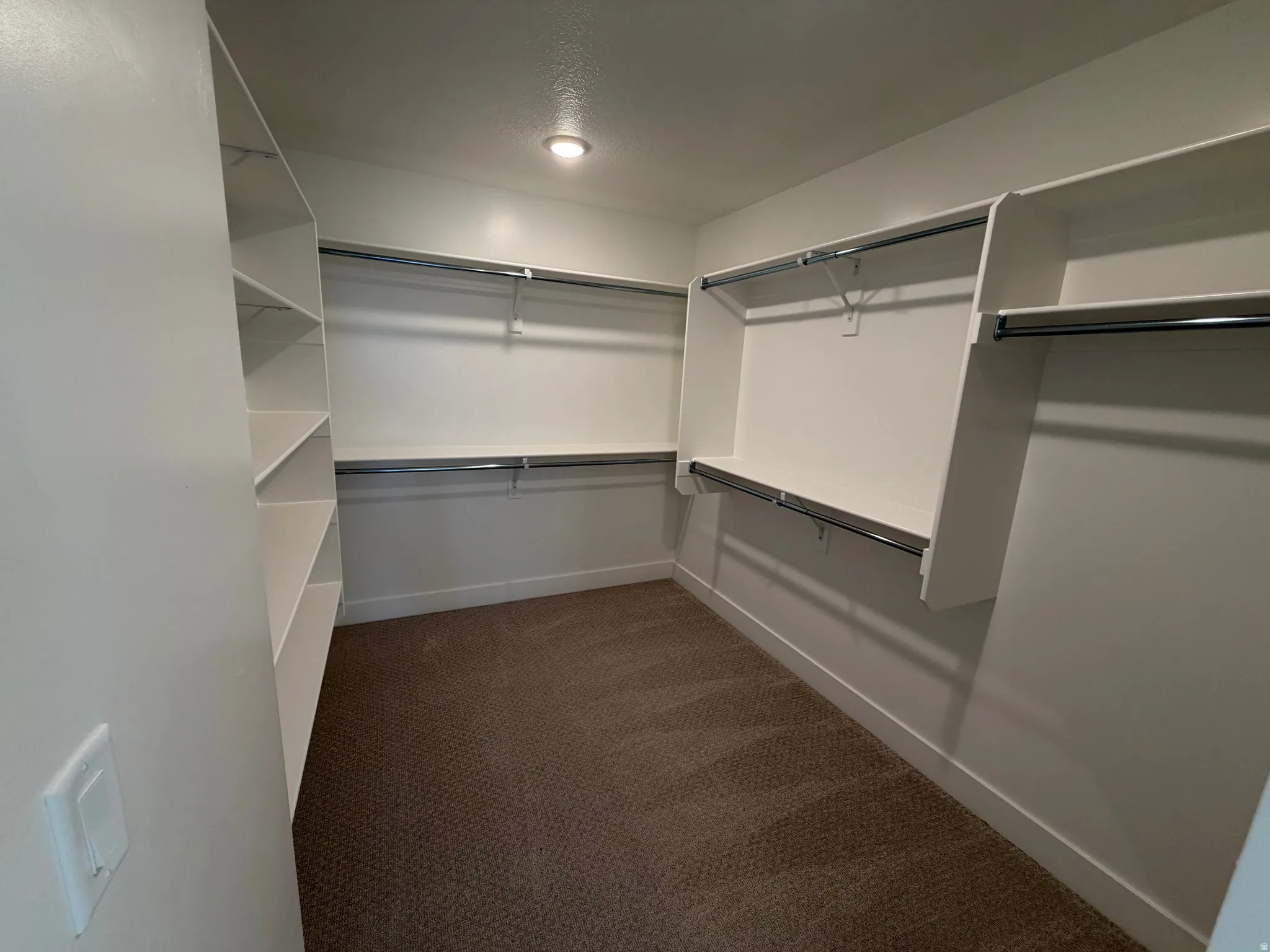 Spacious walk-in closet featuring built-in shelving, multiple hanging rods, recessed lighting, and carpet flooring
