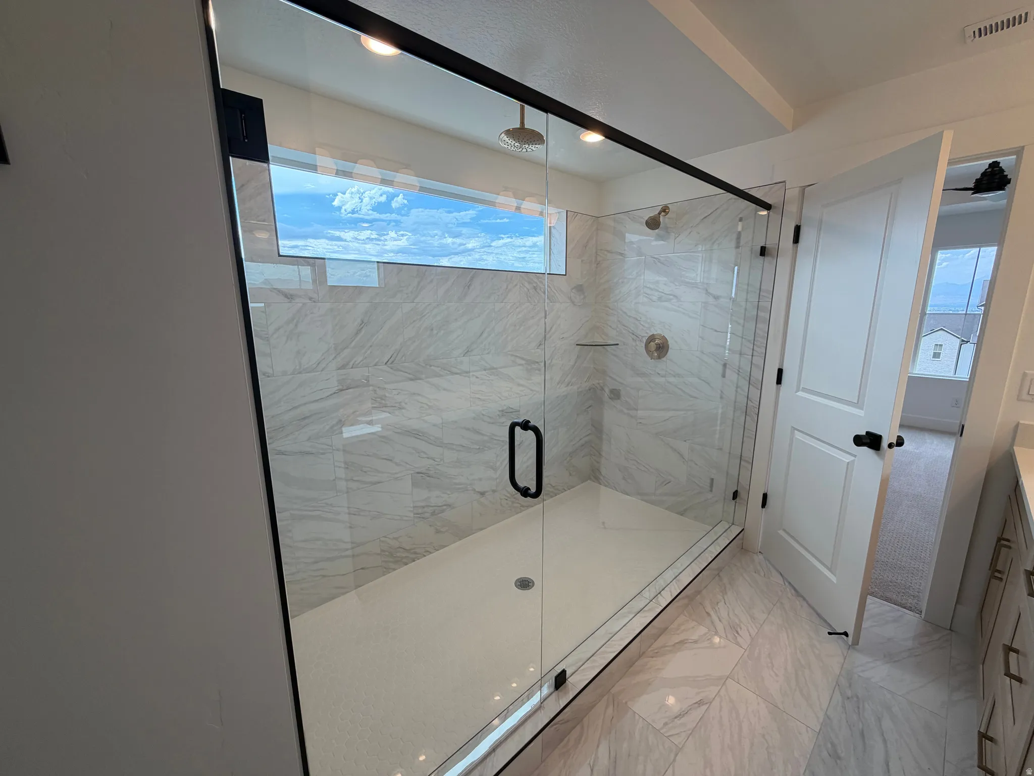 Expansive walk-in shower featuring clear glass enclosure, matte black hardware, rainfall showerhead, and white-veined tile surround