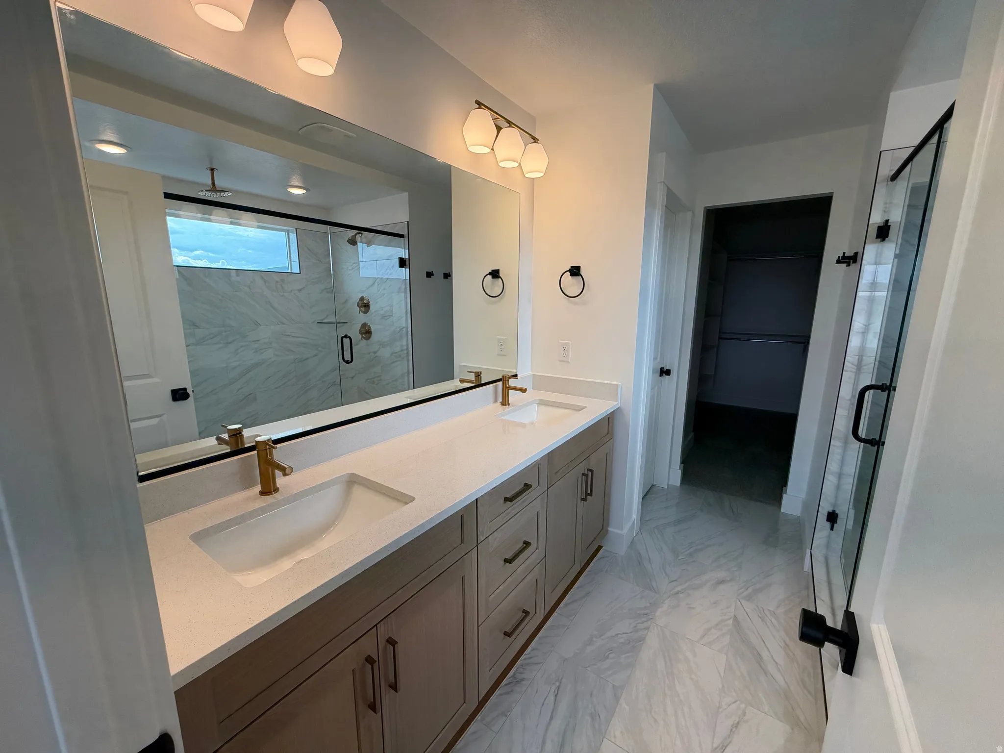 Dual vanity with light-toned cabinetry, white countertops, and gold-finish fixtures