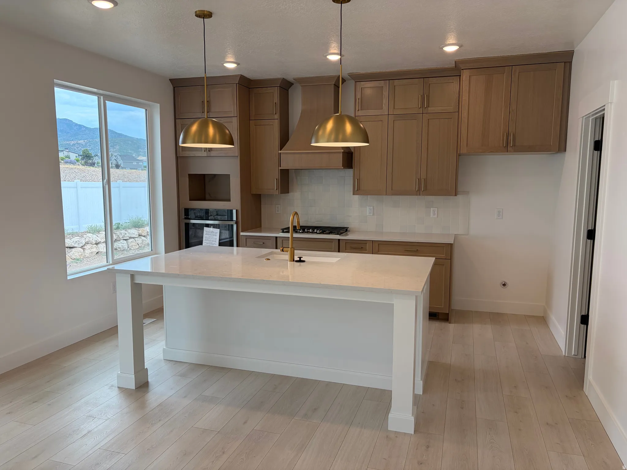 Modern kitchen featuring a white center island with a light-toned countertop, flanked by two brass pendant lights