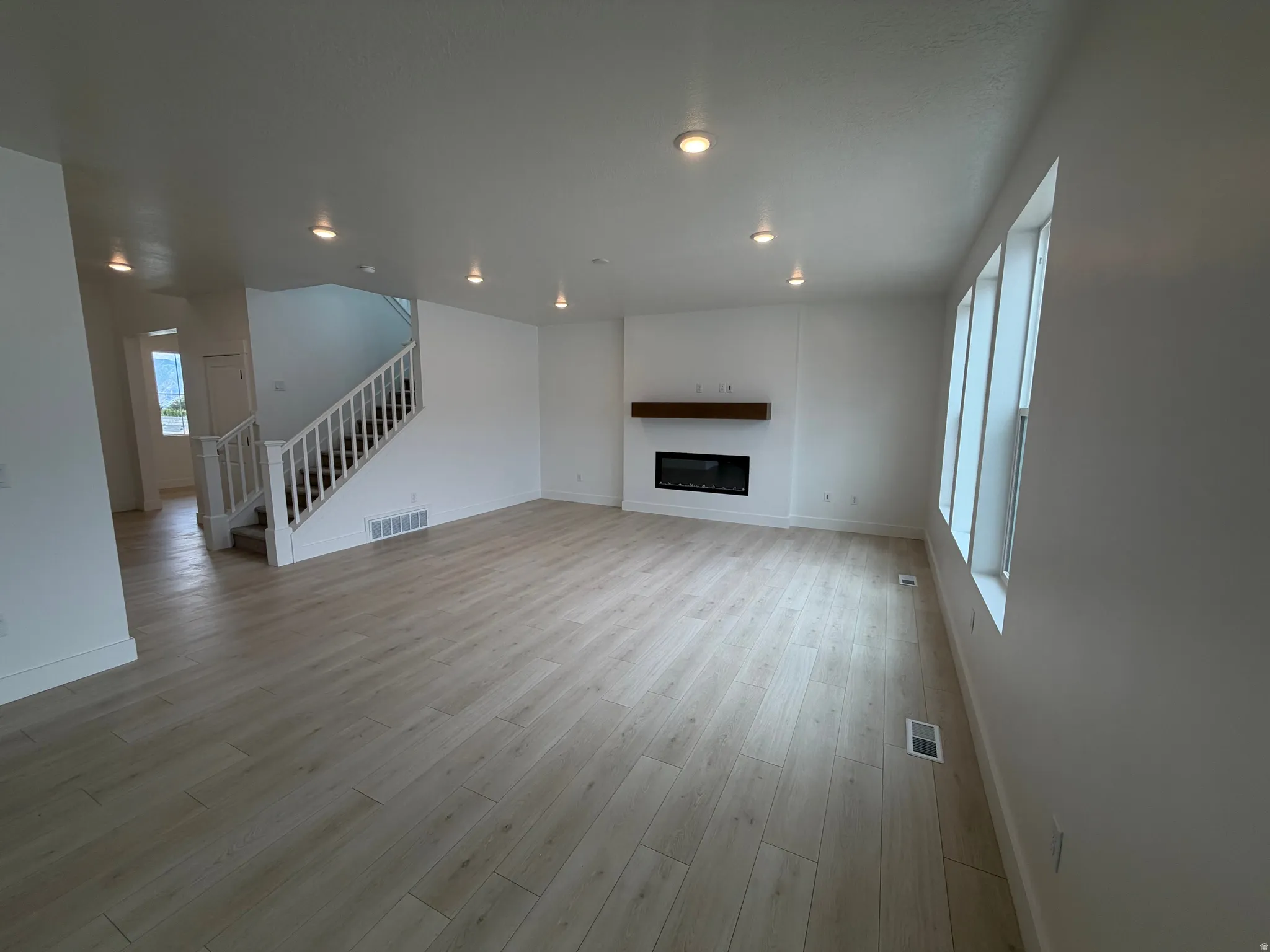 Spacious living area featuring wood-finish flooring, a modern electric fireplace with a wood mantle, and recessed ceiling lighting