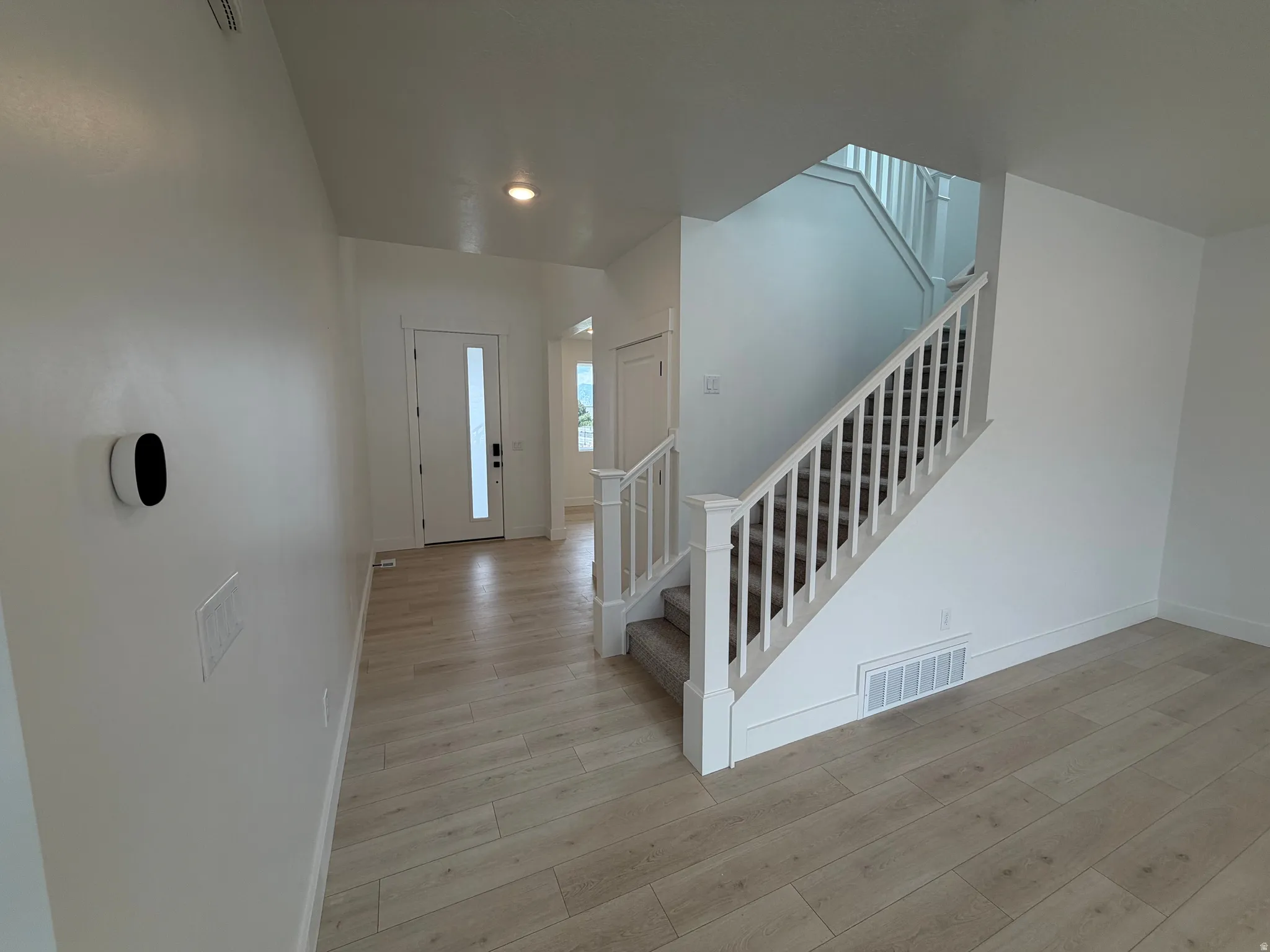 Foyer featuring light wood-finish flooring, a white paneled entry door with frosted glass insert, and a staircase with white balusters and carpeted treads