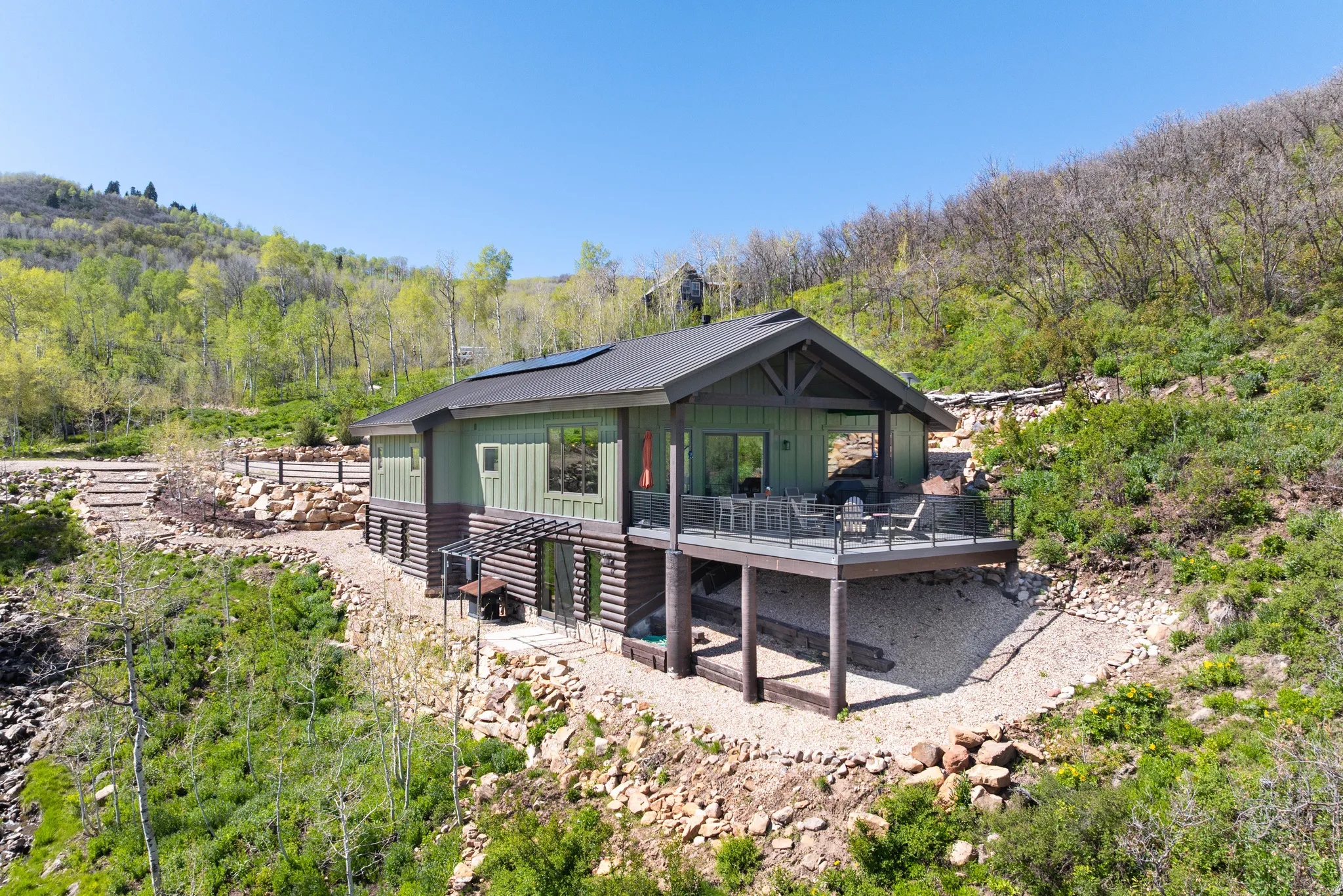 View of front of house featuring solar panels, a deck, board and batten siding, a wooded view, and a patio