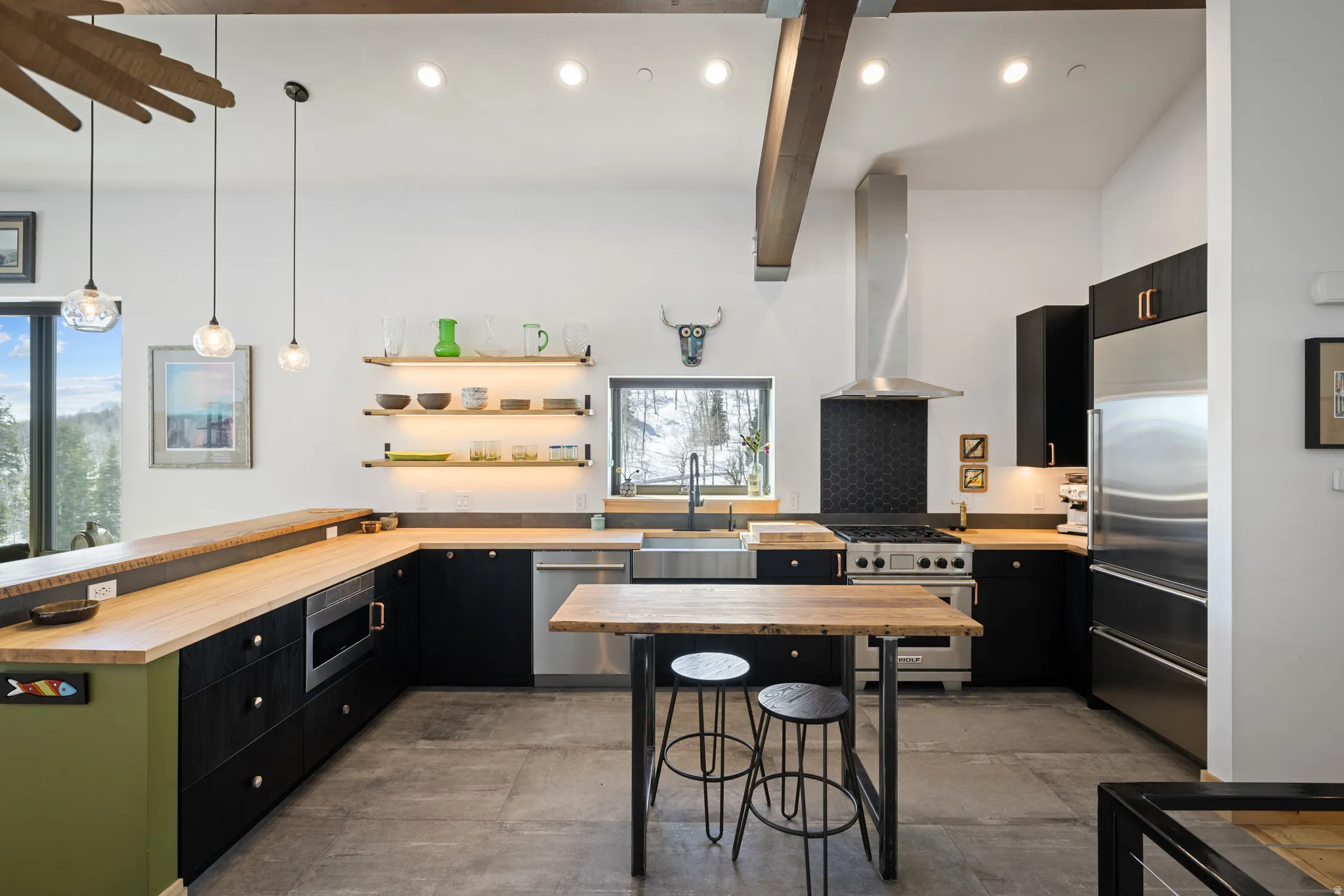 Kitchen with dark cabinetry, a peninsula, built in appliances, wooden counters, and hanging light fixtures