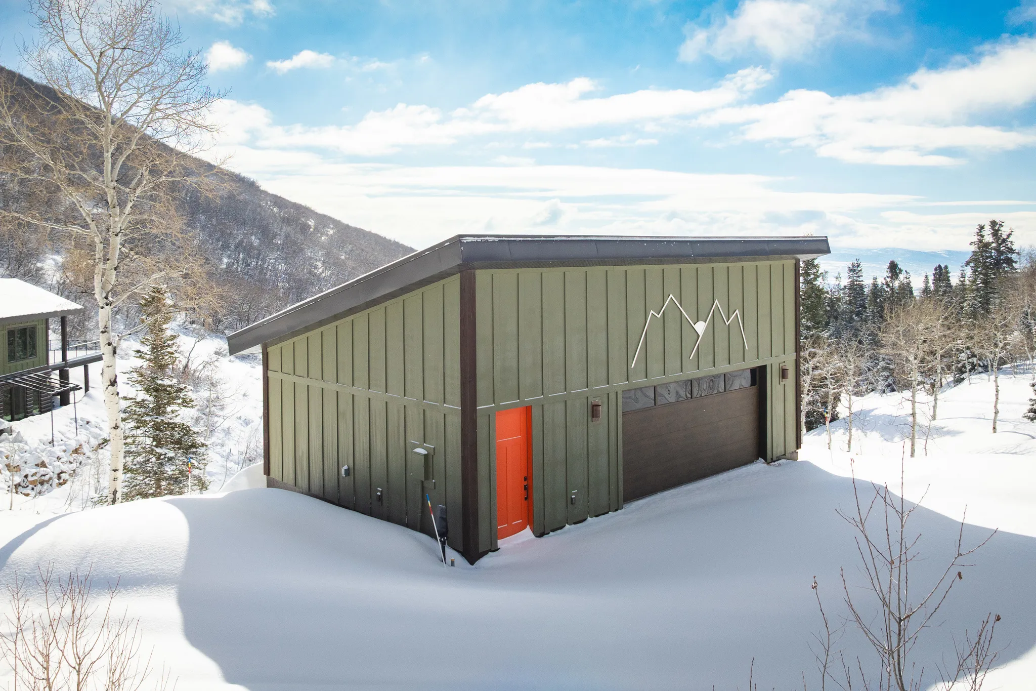 View of snowy exterior featuring board and batten siding, an outdoor structure, and a garage