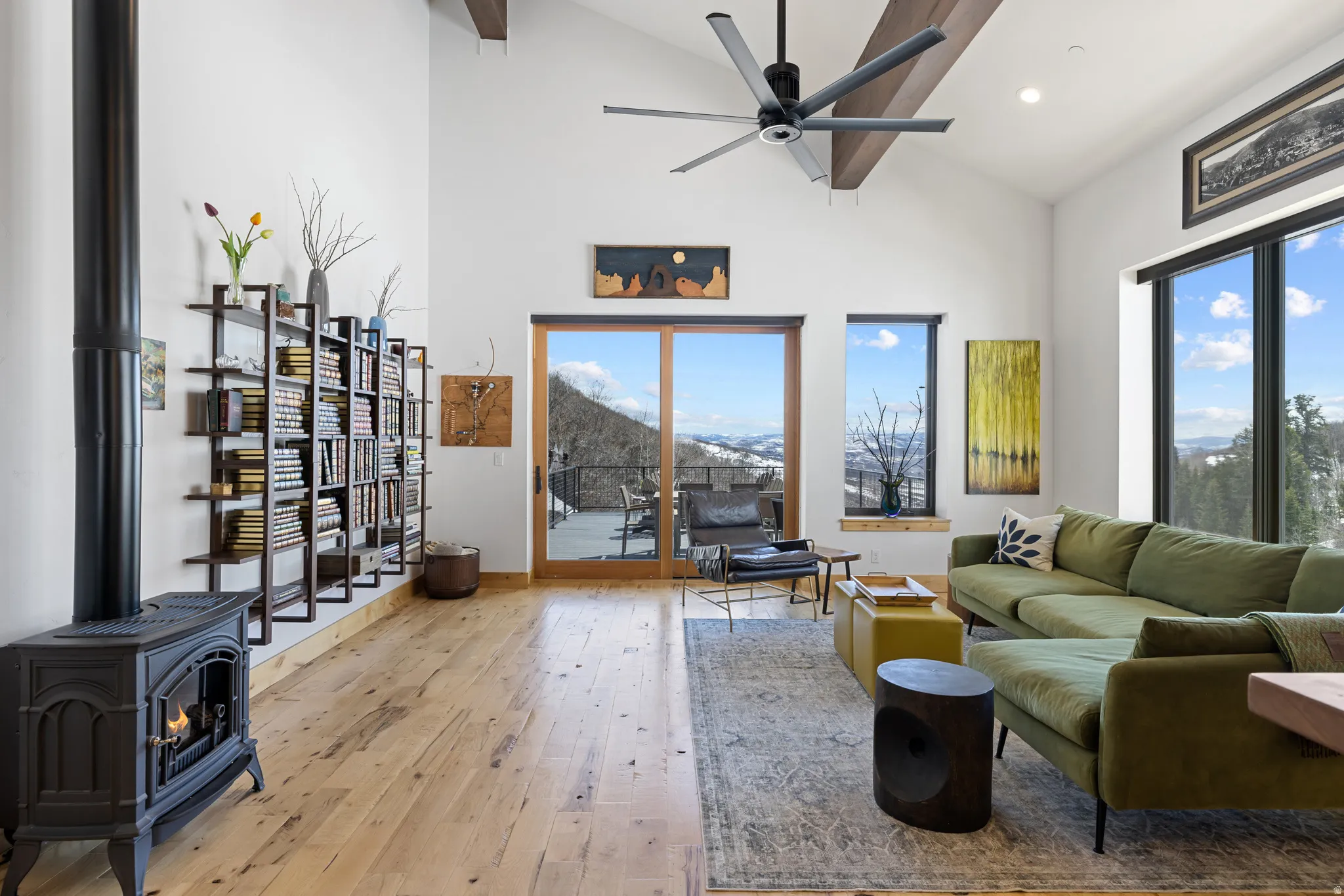 Living room featuring light wood finished floors, a wood stove, lofted ceiling, a ceiling fan, and a mountain view