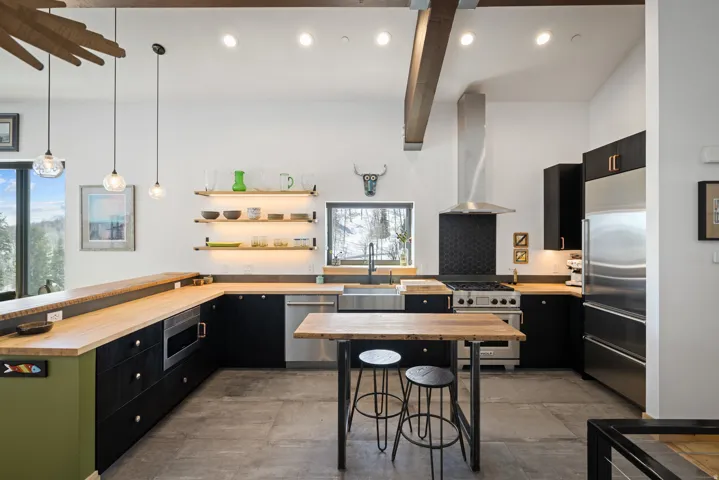 Kitchen with dark cabinetry, a peninsula, built in appliances, wooden counters, and hanging light fixtures