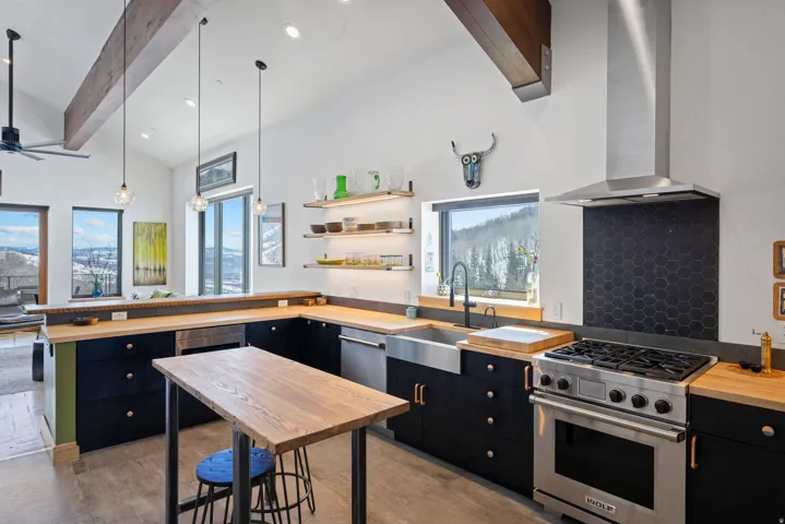 Kitchen with dark cabinetry, stainless steel appliances, a peninsula, wood counters, and open shelves