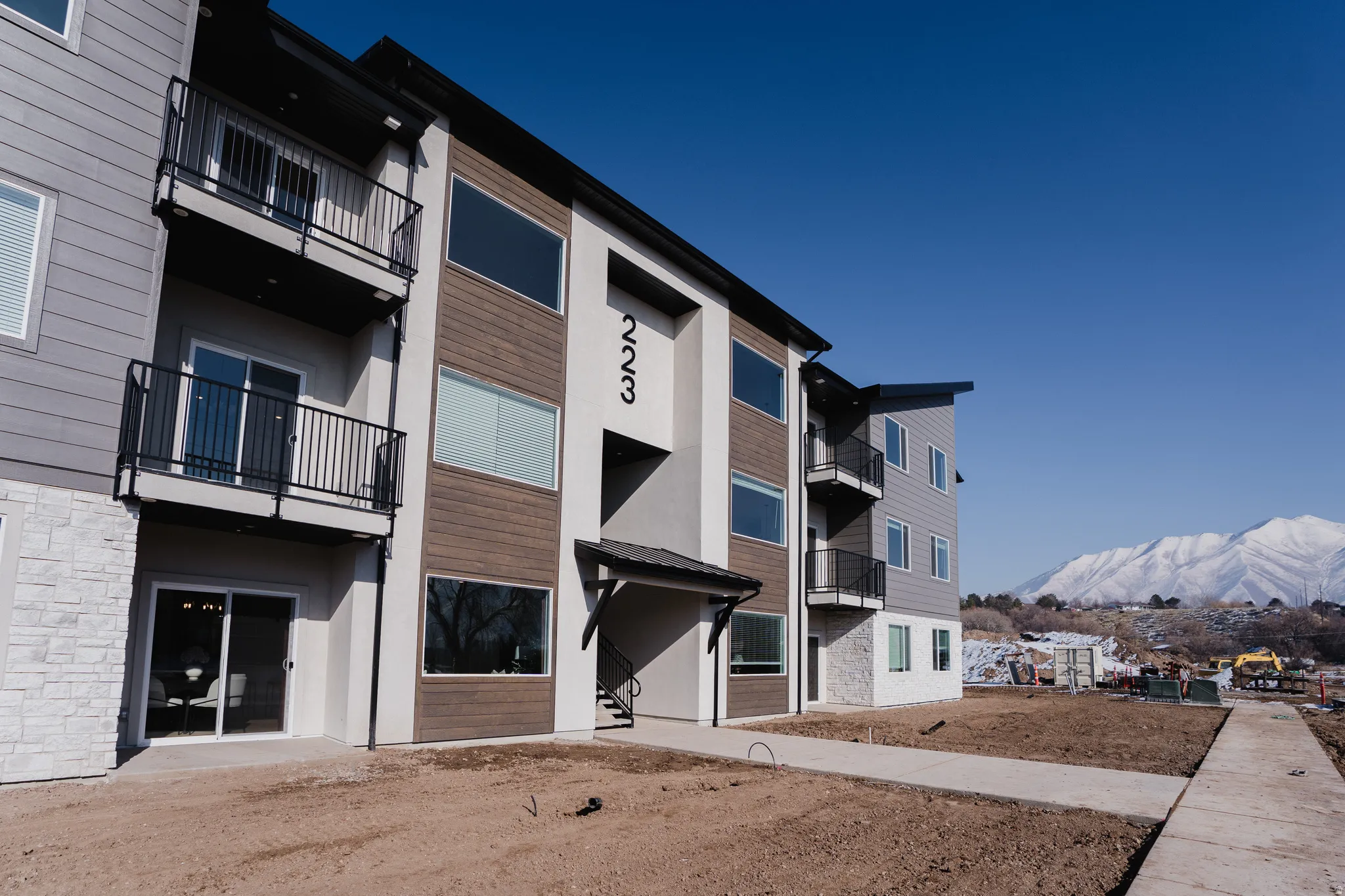 Modern multi-story building featuring balconies with black railings, horizontal siding, and a stone facade