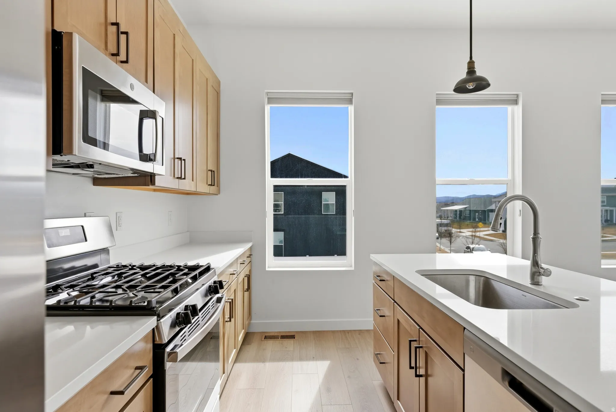 Kitchen featuring stainless steel appliances, light stone counters, light wood-type flooring, pendant lighting, and light wood finish cabinets