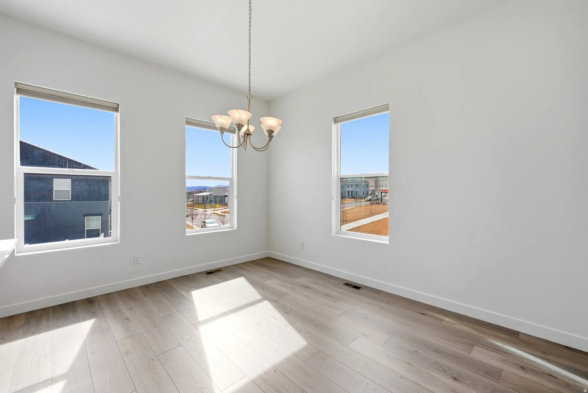 Unfurnished room with suspended lighting and light wood-style flooring