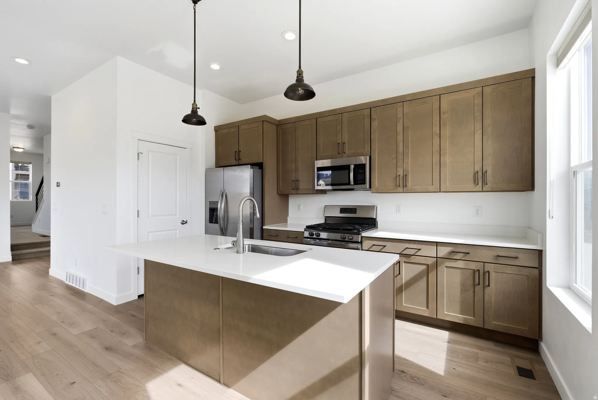 Kitchen featuring stainless steel appliances, an island with sink, decorative light fixtures, and light wood finished floors