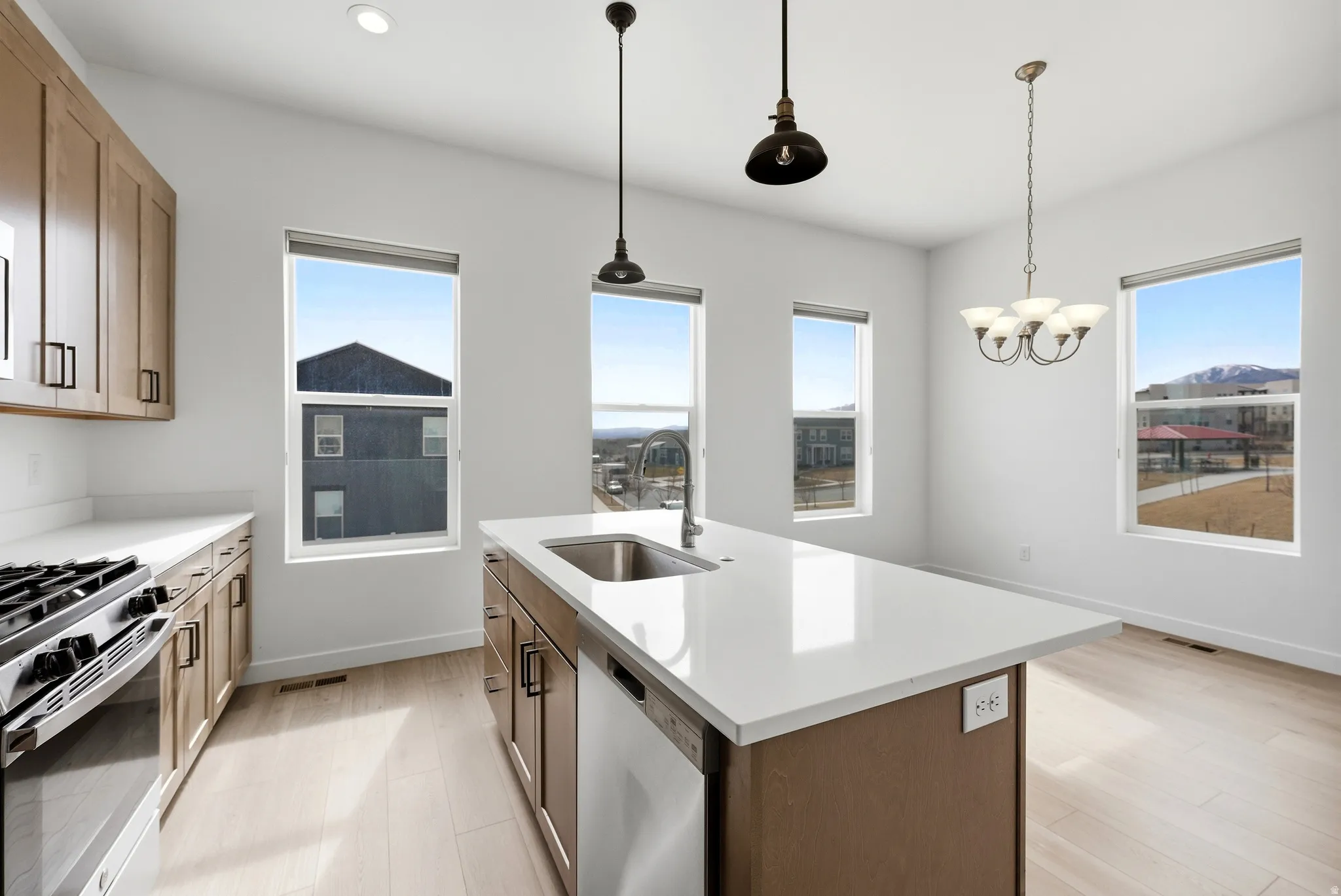 Kitchen with stainless steel appliances, a center island with sink, light wood-style flooring, hanging lights, and healthy amount of natural light