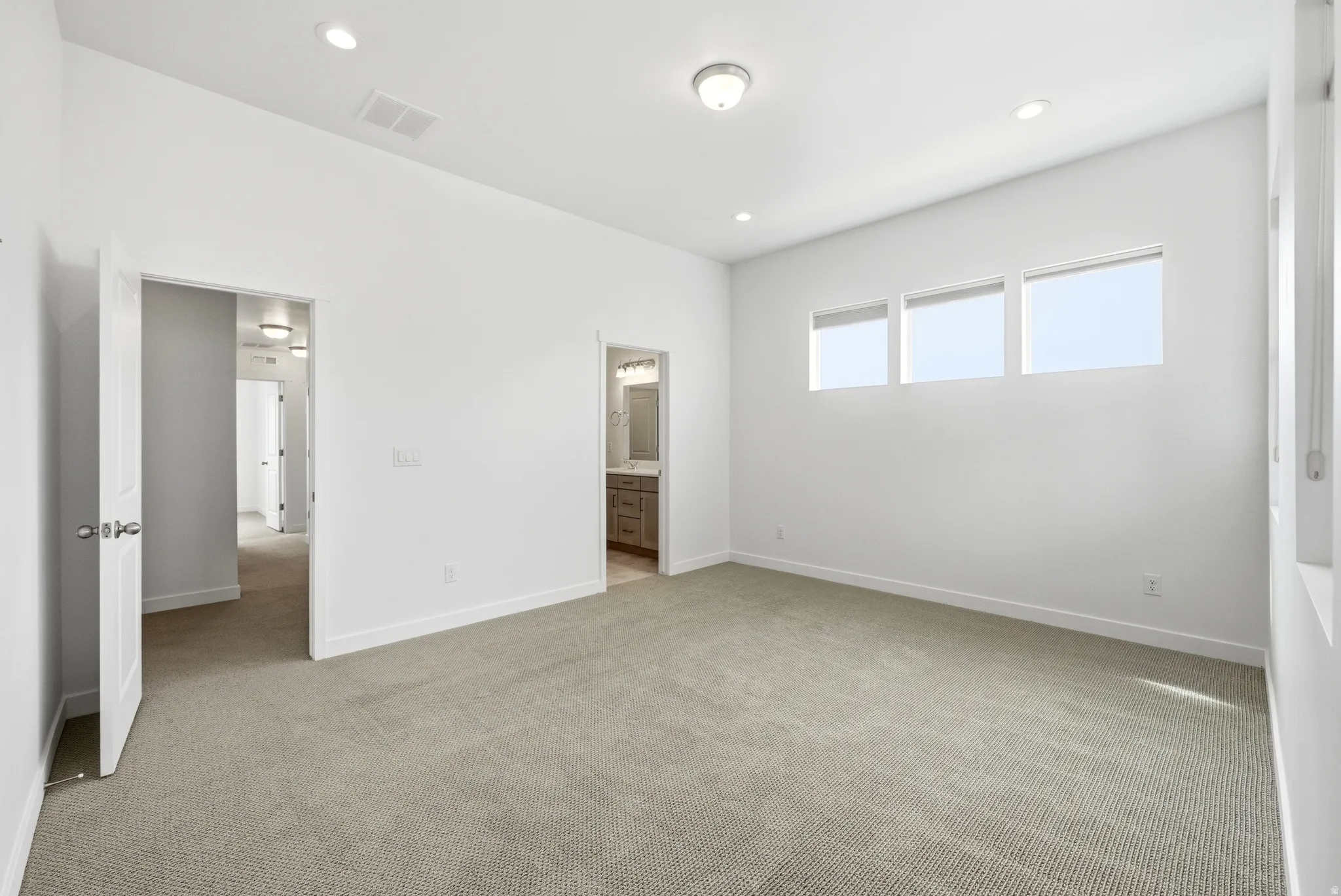 Unfurnished bedroom featuring light carpet, ensuite bath, and recessed lighting