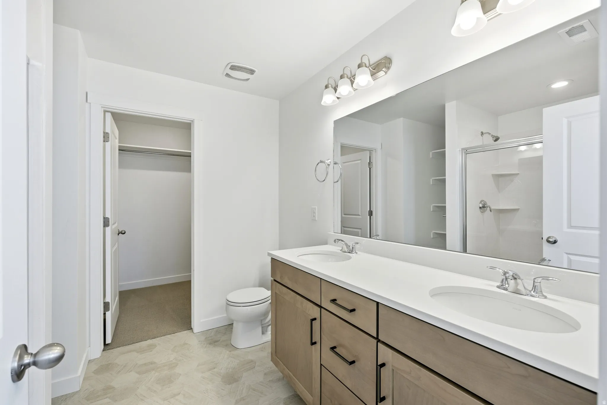 Bathroom with a stall shower, double vanity, and a walk in closet