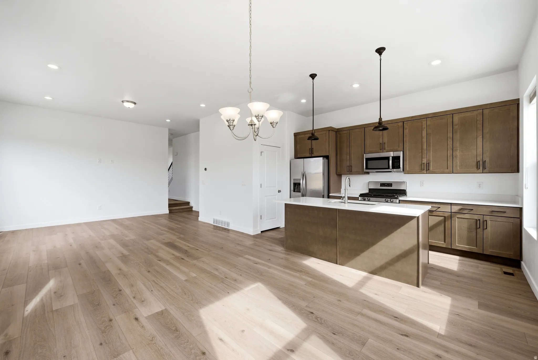 Kitchen with a chandelier, light wood-style floors, a kitchen island with sink, stainless steel appliances, and open floor plan