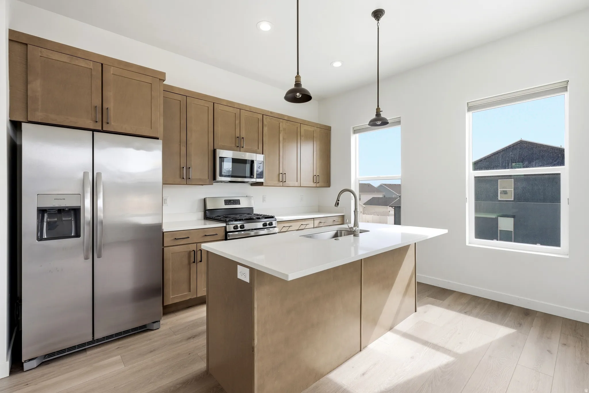 Kitchen featuring stainless steel appliances, a center island with sink, light wood-style floors, and decorative light fixtures