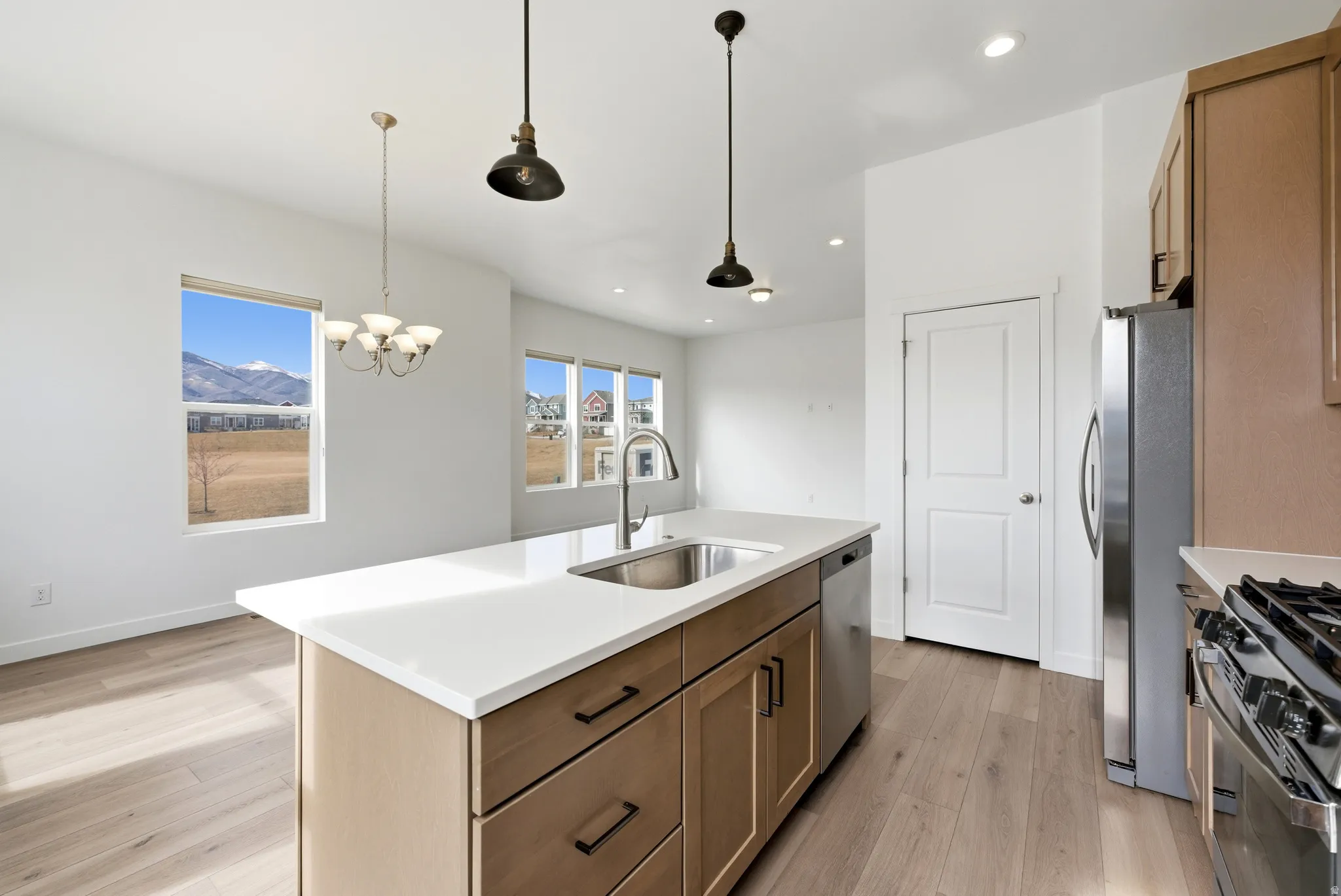 Kitchen with light wood-style floors, a center island with sink, stainless steel appliances, wood finish cabinetry, and light stone countertops