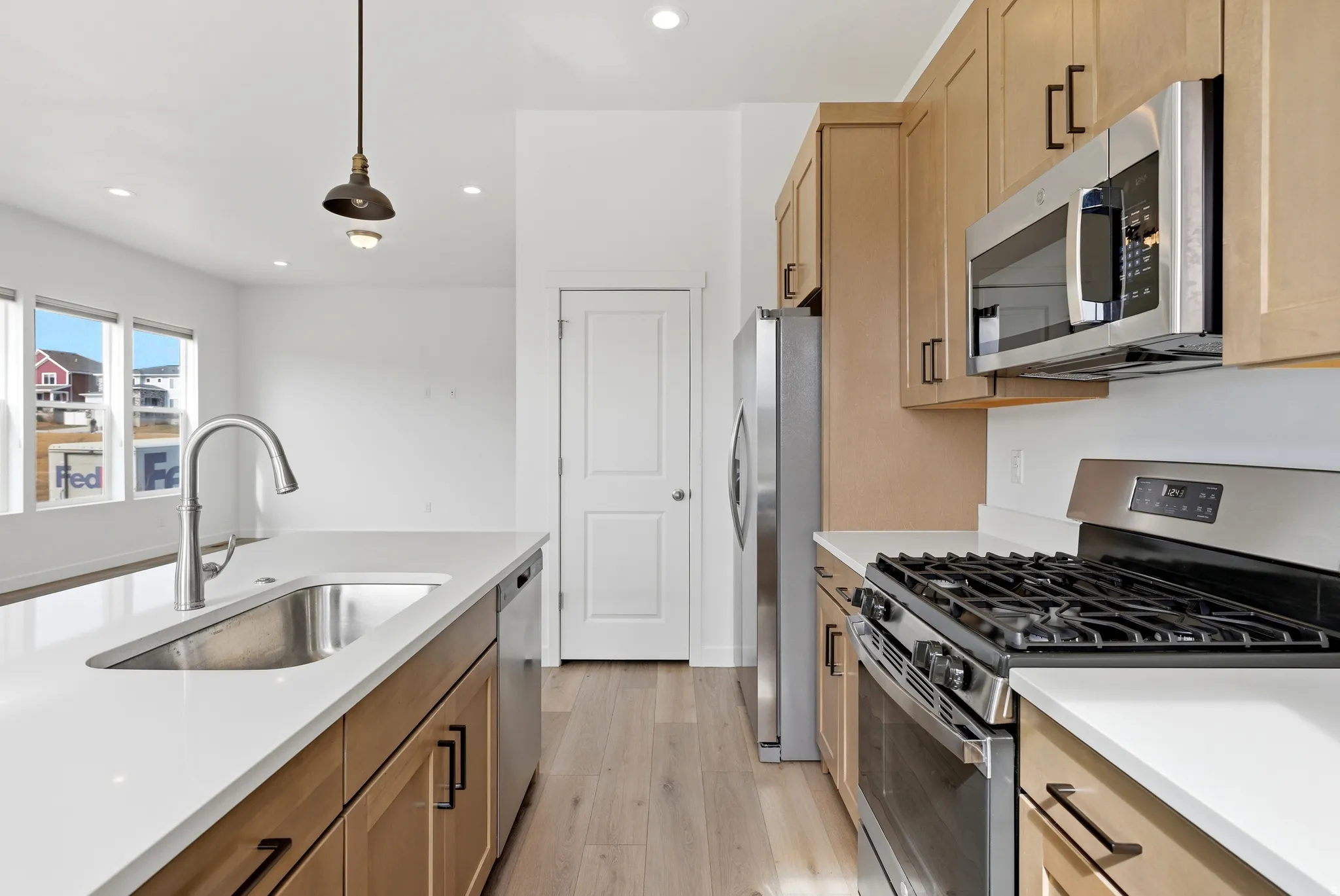 Kitchen featuring stainless steel appliances, light wood-style flooring, hanging light fixtures, light stone countertops, and light wood finish cabinetry