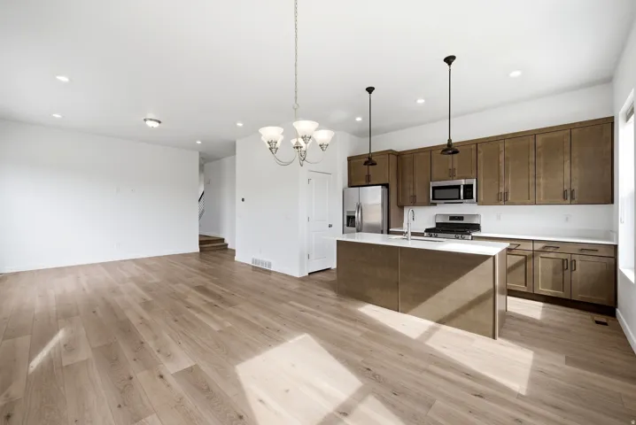 Kitchen with a chandelier, light wood-style floors, a kitchen island with sink, stainless steel appliances, and open floor plan