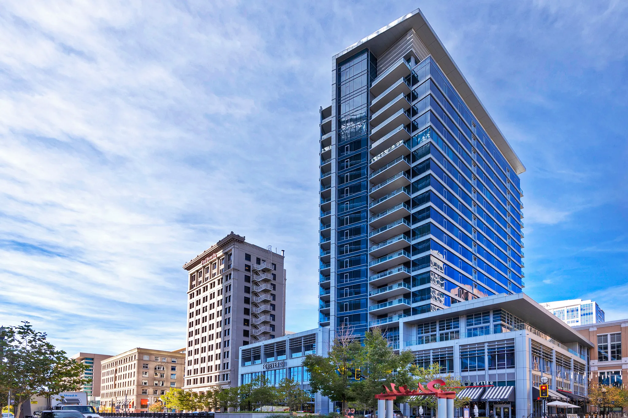 Modern high-rise building featuring extensive glass curtain walls, multiple private balconies, and a distinctive rooftop overhang