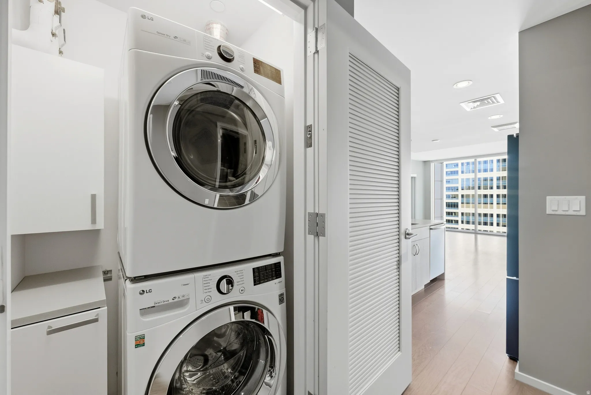 Dedicated laundry area featuring stacked front-load washer and dryer, white cabinetry, and light-toned countertop