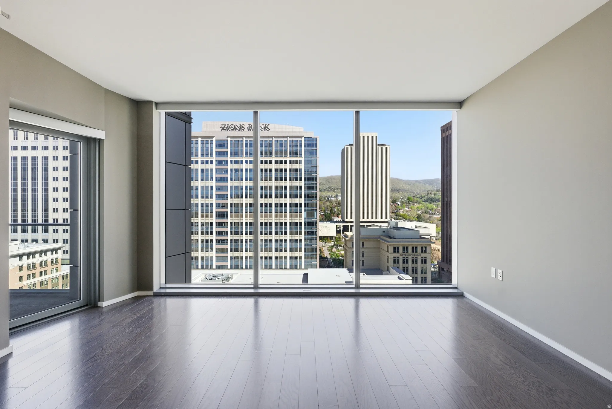 Spacious room featuring floor-to-ceiling windows, dark wood-finish flooring, and a sliding glass door opening to a balcony
