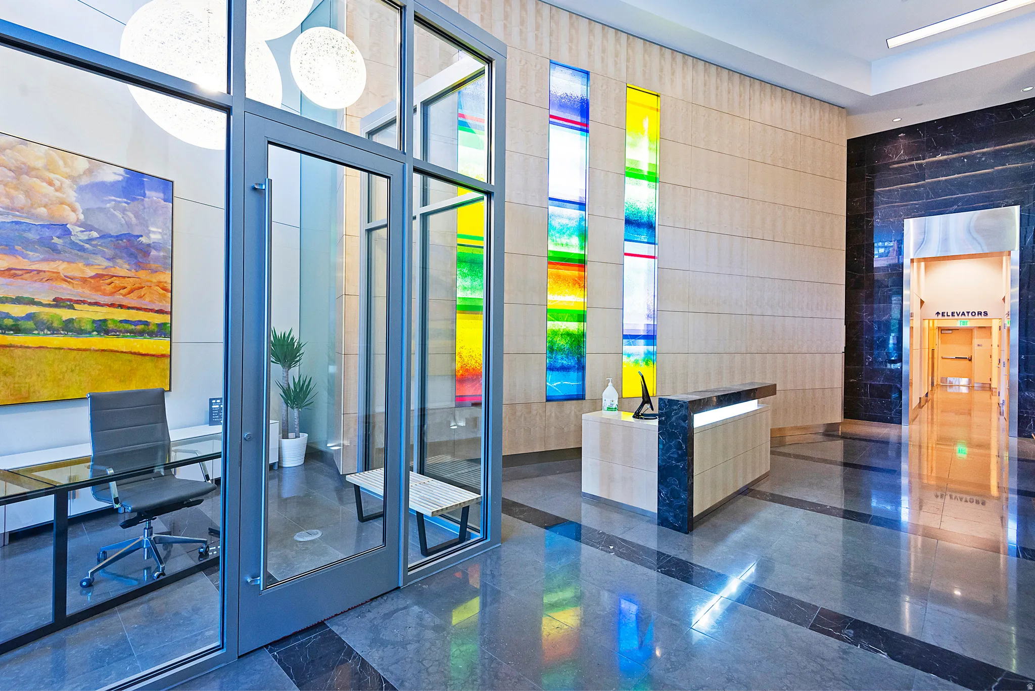 Spacious lobby featuring polished stone flooring, a contemporary reception desk, decorative stained glass wall panels, and an enclosed office space with glass walls