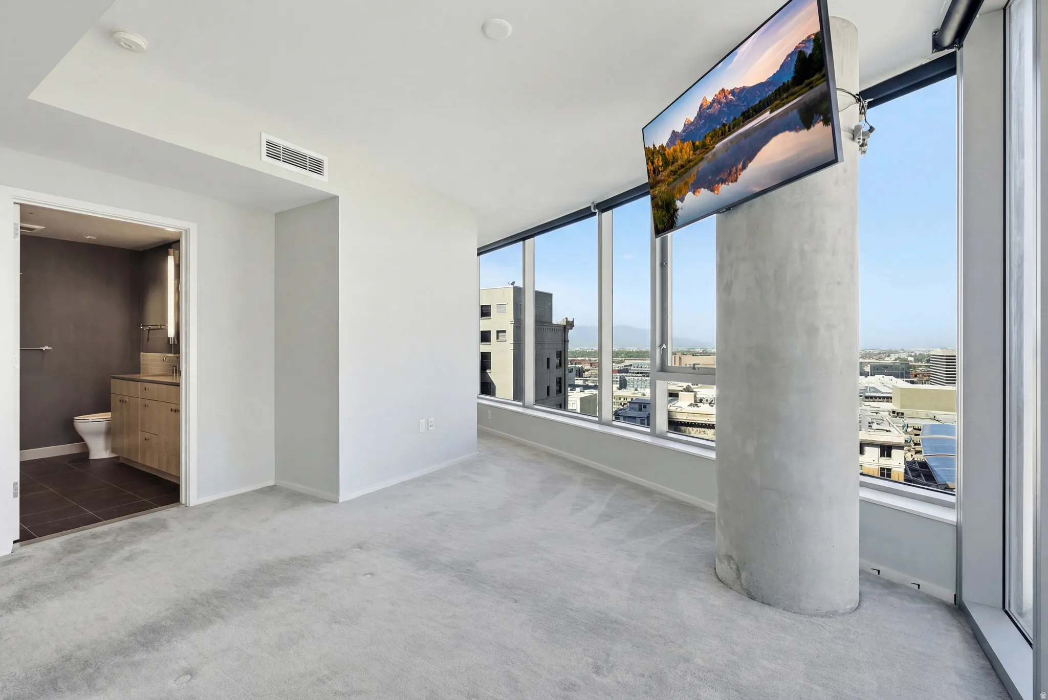 Light gray carpeted room featuring a concrete pillar and expansive window walls offering urban scenery