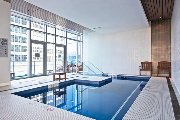 Indoor swimming pool featuring blue mosaic tiling and a white tiled surround