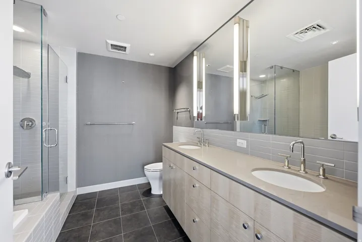 Bathroom featuring a glass-enclosed shower, dual vanity with undermount sinks, and a full-length mirror with integrated vertical lighting