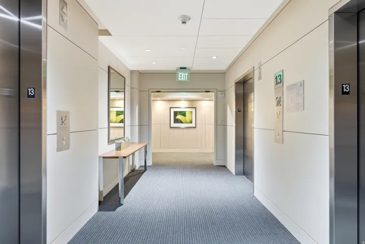 Hallway featuring two stainless steel elevators, recessed lighting, carpet flooring, and a console table with a mirror