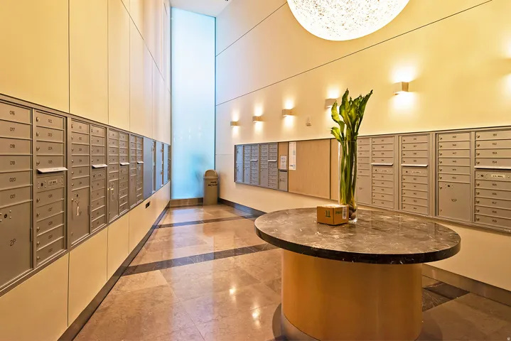 Mailroom featuring extensive wall-mounted mailboxes, a central oval table with a dark stone-finish top, and integrated wall lighting