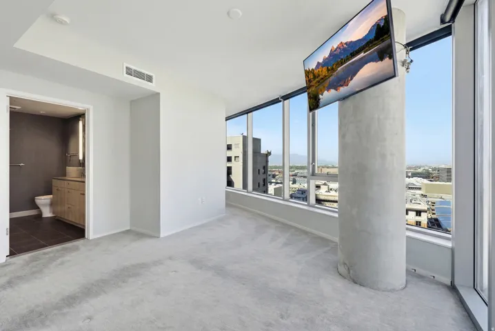 Light gray carpeted room featuring a concrete pillar and expansive window walls offering urban scenery