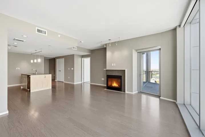 Open-concept living area featuring wood-finish flooring, a contemporary fireplace with a fluted surround, and a kitchen island with pendant lighting