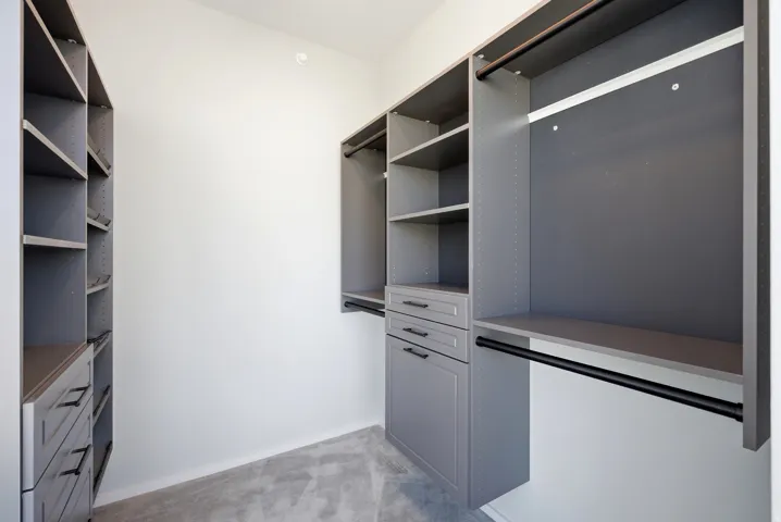 Custom storage system featuring gray cabinetry, integrated shelving, three drawers with dark hardware, and multiple hanging rods