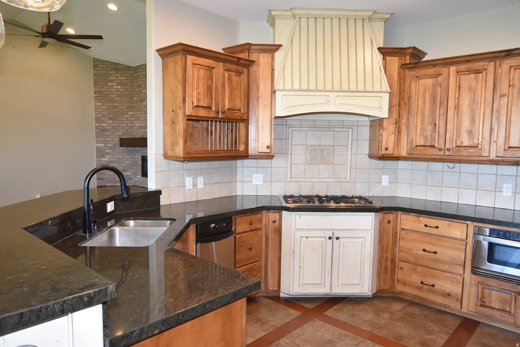 Kitchen featuring dark countertops, wood cabinetry, stainless steel dishwasher, built-in microwave, and a gas range with custom hood