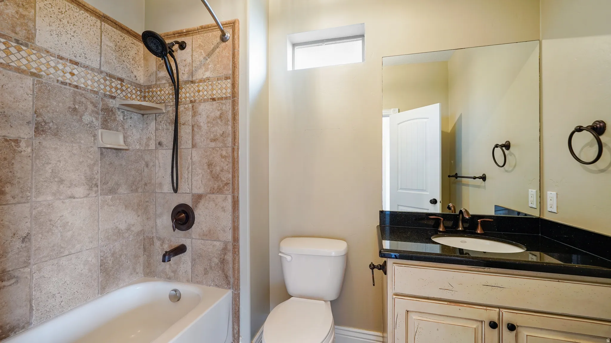 Bathroom featuring a tile-surround tub/shower combination with mosaic accent, dark bronze fixtures, a vanity with distressed cabinetry, a dark countertop, and a rectangular undermount sink
