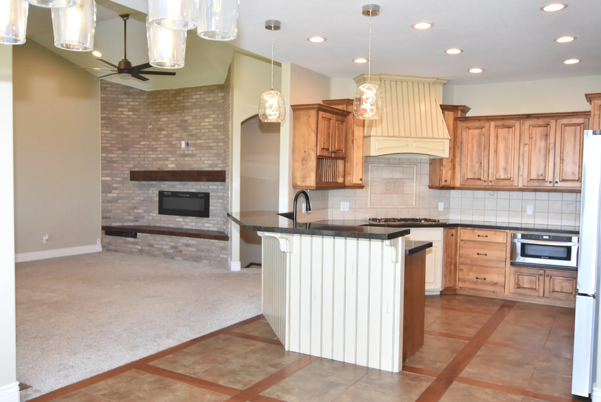 Open-concept living space featuring a gas fireplace with brick surround, vaulted ceiling, and recessed lighting