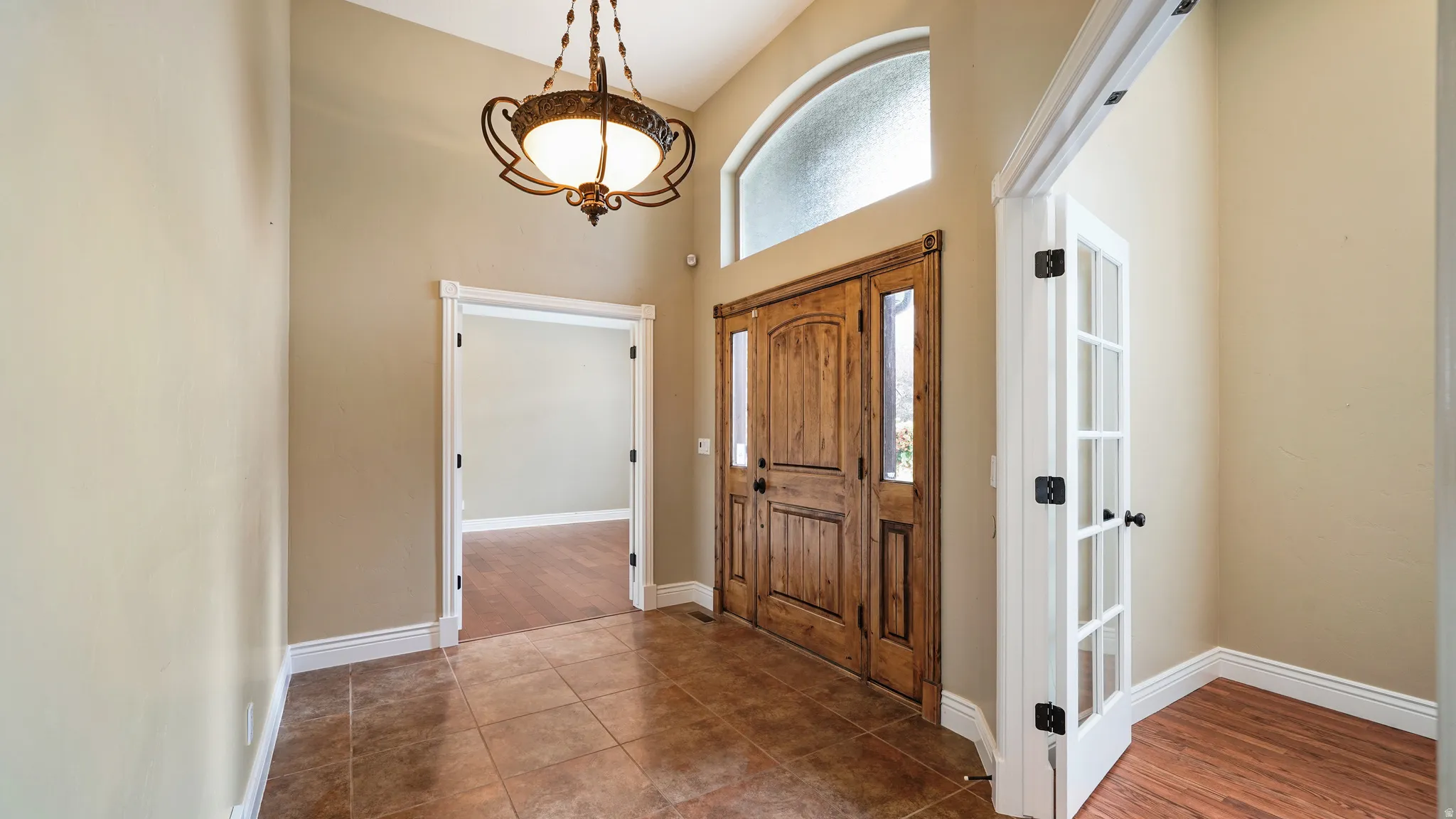Inviting foyer featuring a double wood-paneled entry door, arched transom window, and a decorative overhead light fixture