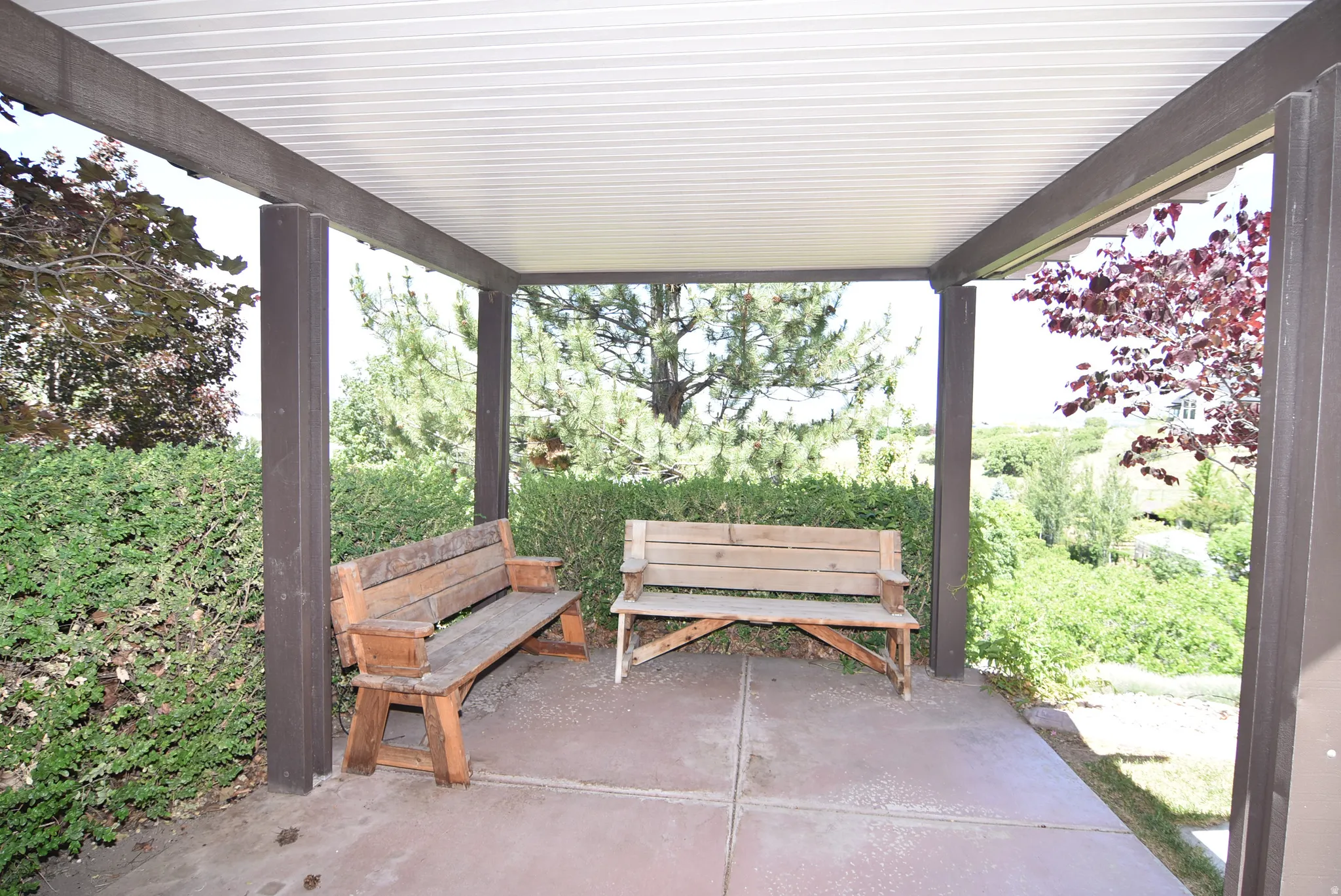 Covered gazebo with a solid roof structure, dark-toned support beams, and a concrete slab floor