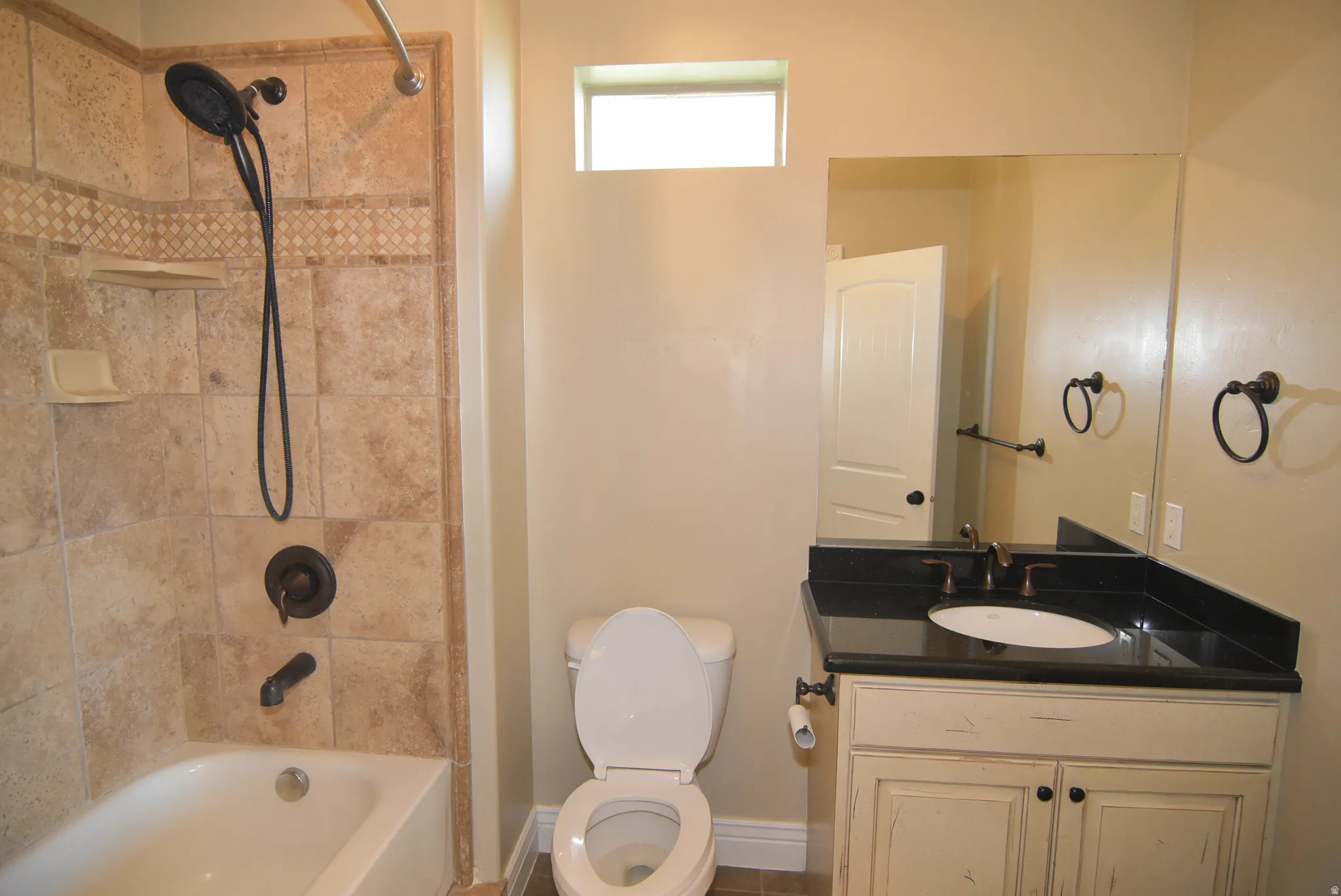 Main bathroom featuring a tiled tub/shower combination with mosaic accent, oil-rubbed bronze fixtures, a vanity with a dark countertop, an undermount sink, and a framed mirror