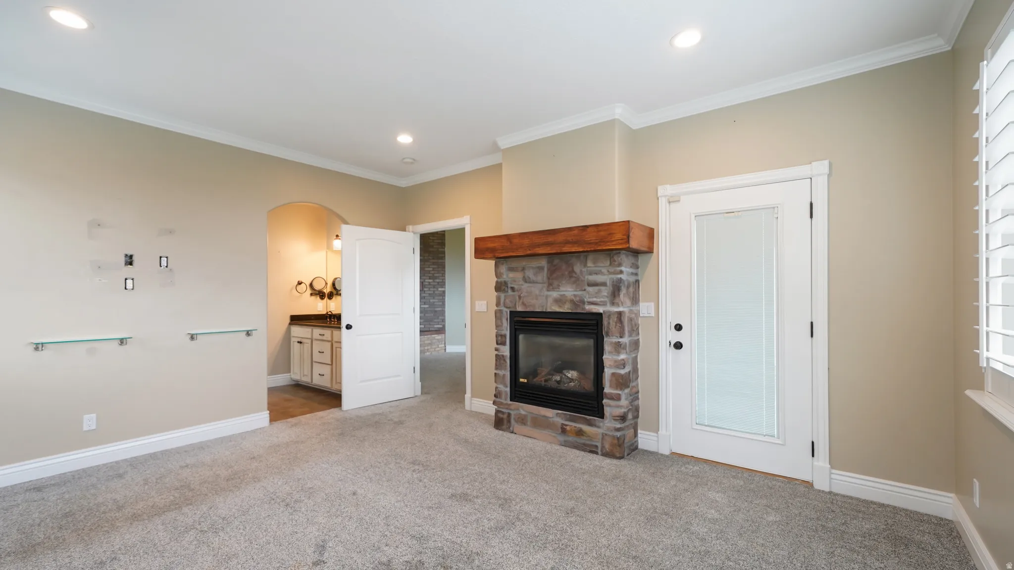 Spacious room featuring a stone-faced fireplace with a wood mantel, crown molding, recessed lighting, and soft gray carpeting